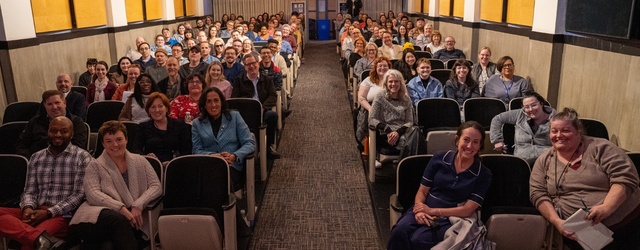 A staff photo. A large group of employees sitting in a movie theater smiling.