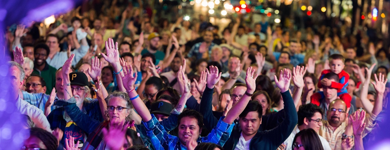 a crowd of people raise their hands