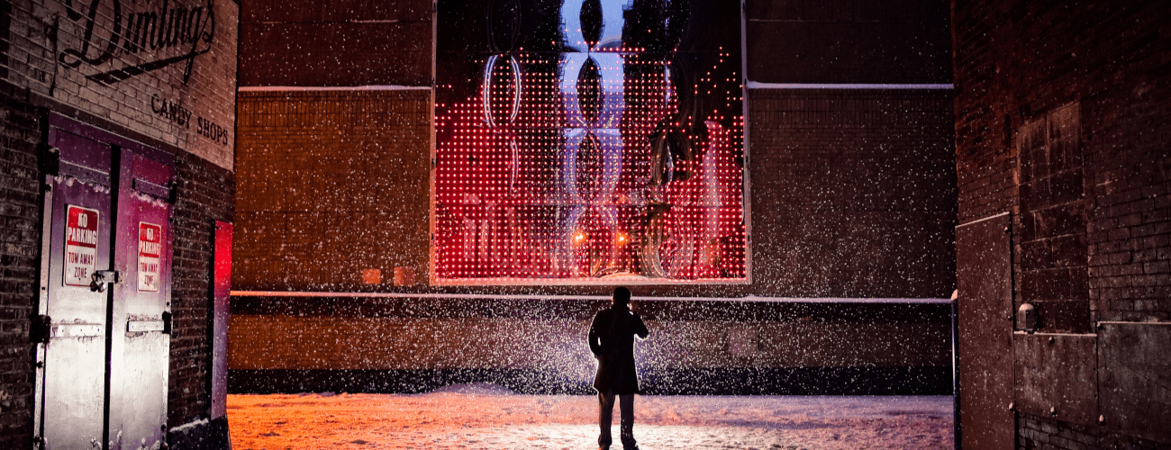 person standing in front of light art piece in an alley