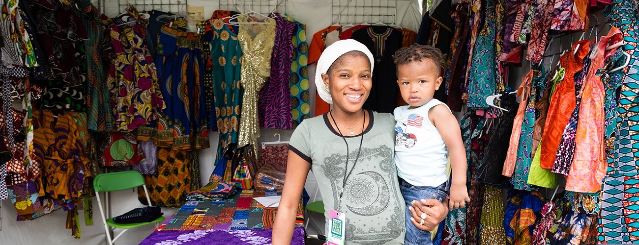 woman with baby standing in front of booth displaying textile art