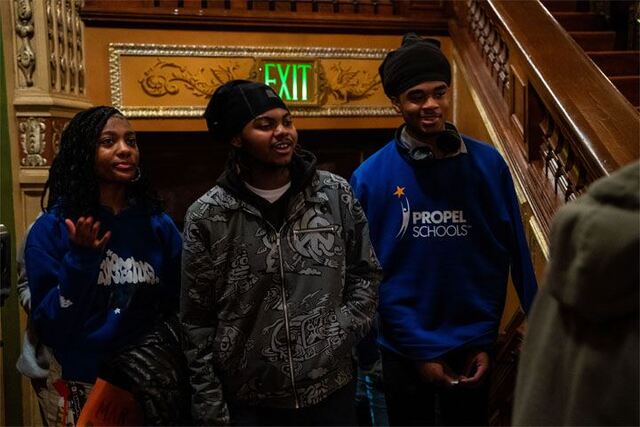  Three highschooler walk into the Benedum Center auditorium. One student is wearing a Propel Schools sweatshirt.