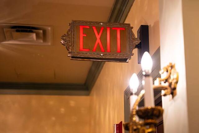 An exit sign with glowing red letters and encased in an ornate mold sticks out of the wall.