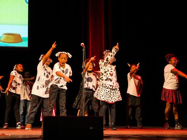 A group of middle school students dressed in spotted Dalmatian costumes sing on stage.