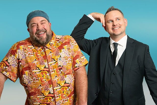 Two men pose side by side. One man is mid laugh while the other man rests his arm on his shoulder.