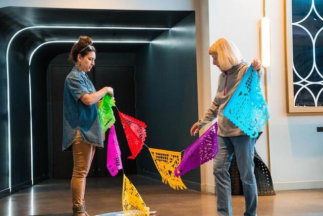 Two women hold up a string of multi-colored papel picado.