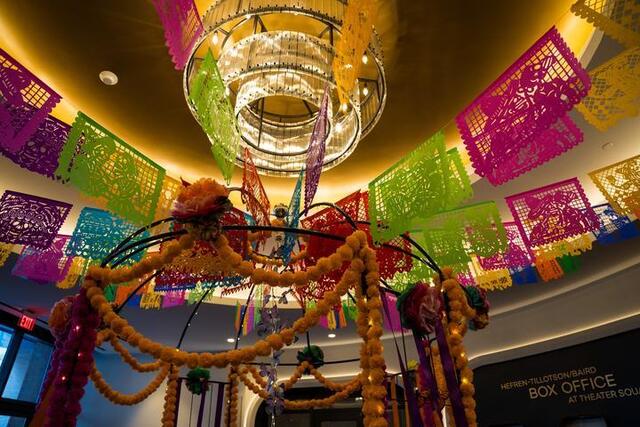 Papel picado and orange marigolds frame the ceiling and chandelier in the Kara Family Lobby.