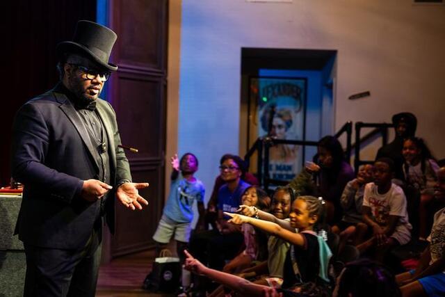 Joshua Messado holds out his hand to show an empty palm. The children point towards his hand.