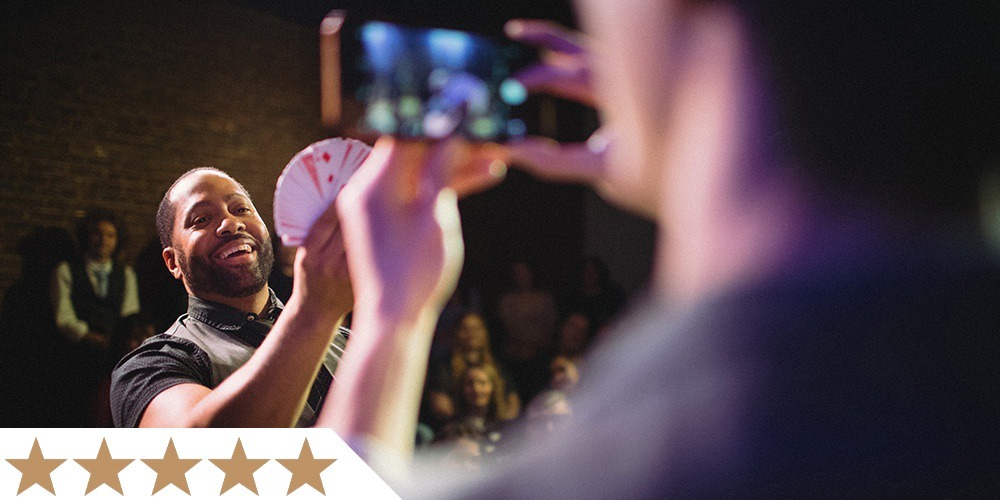 an audience member smiles while holding playing cards as part of an interactive illusion