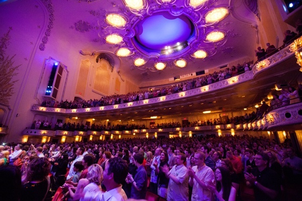 Heinz Hall auditorium with patrons in the seats and balconies beneath an ornate ceiling and house lighting.