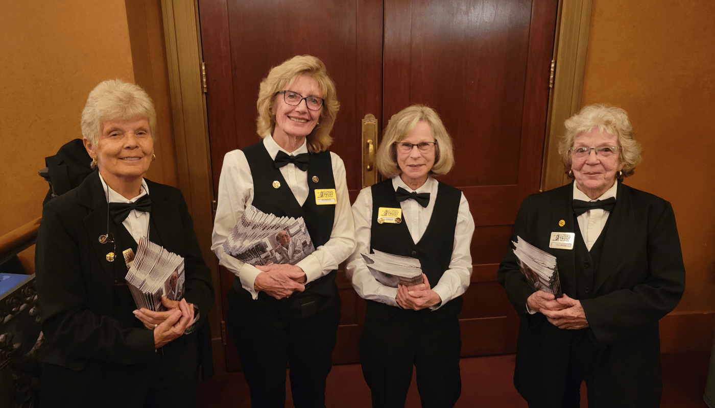 A group of four women in formal, black and white volunteer uniforms hold programs in the Benedum Center.