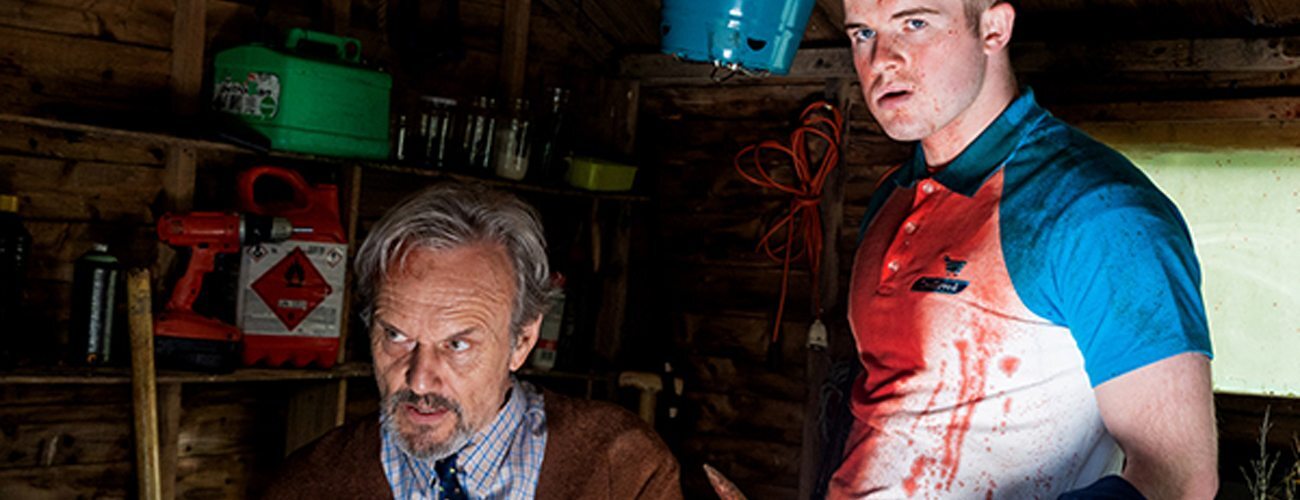 an older man tied up in a chair next to a young man covered in blood, holding a wooden stake