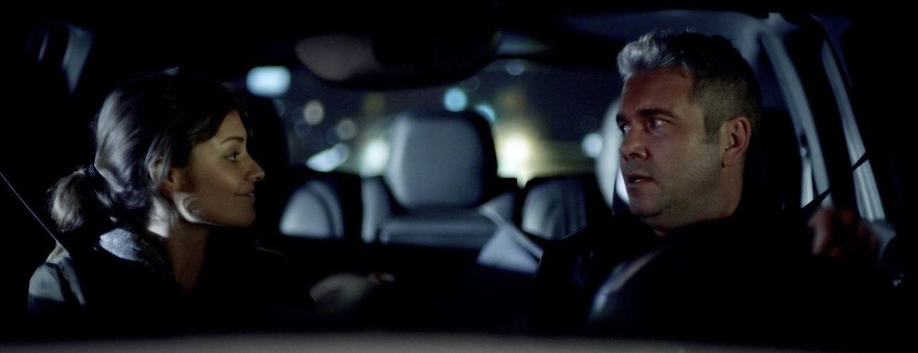 a man and a woman sitting in the front seats of a car looking at eachother