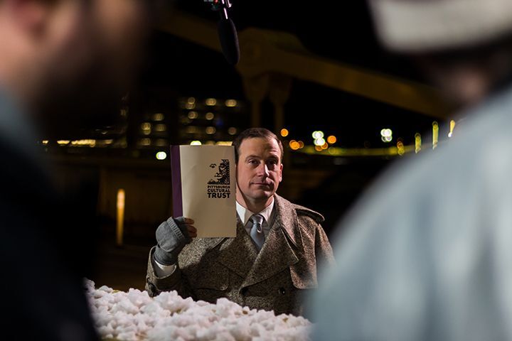 actor portraying the trust logo arty holds up printed logo for comparison