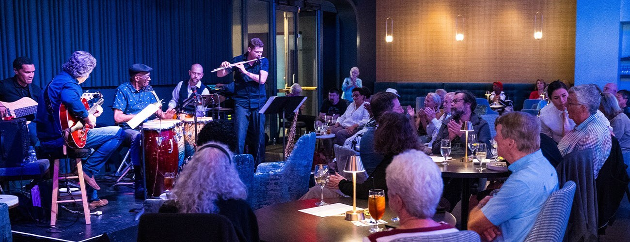 A jazz band playing on a small stage in a restaurant. Audience members watch.
