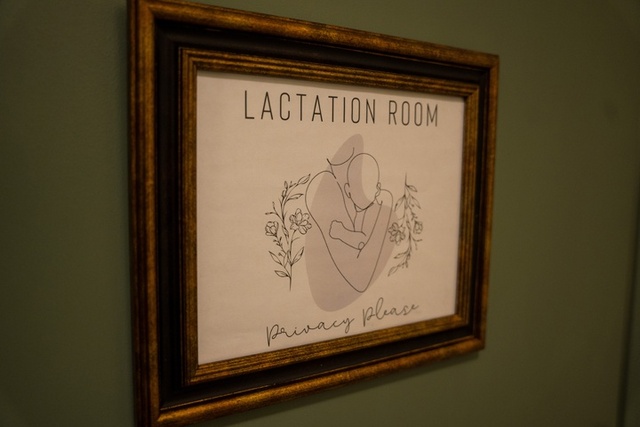 A close up of a print on a green wall. The print says Lactation Room, Privacy Please with a line drawing of person holding a baby.
