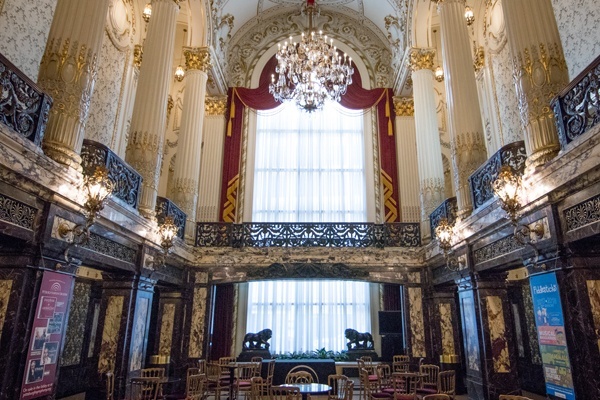 Heinz Hall entrance lobby with marble columns, chandelier, and seating near the grand window.