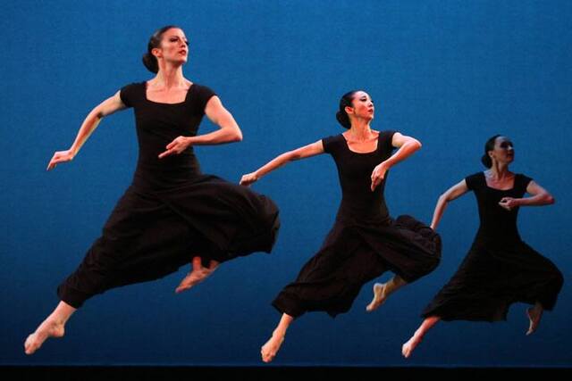 Three women in long black dresses leap into the air.