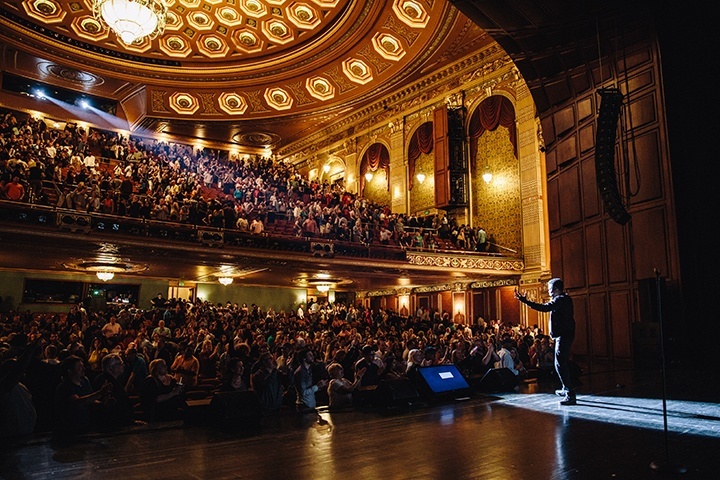 a photo from backstage at the benedum center, looking out at a packed house. comedian chris rock is on stage.