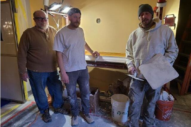 Three men stand beside table with an element of the plaster work.