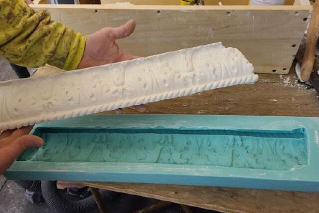 A person holds up a piece of ornate, white plaster molding.