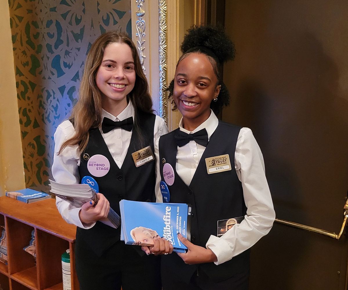 two volunteers holding show programs and smiling.