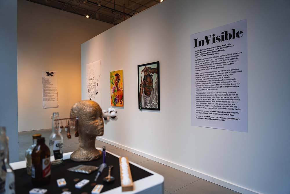 A large vinyl gallery statement hangs on a white gallery wall beside it hang three painted portraits