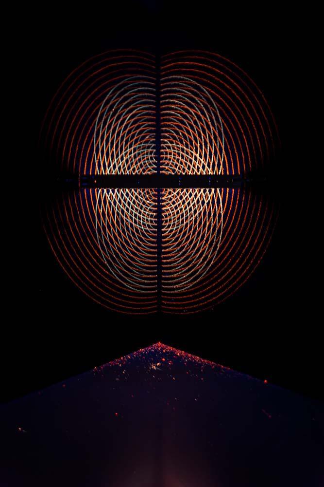 One piece from Gift Shop. A geometric pattern made out of chalk-drawn circles on a black wall is lit up by black lights.