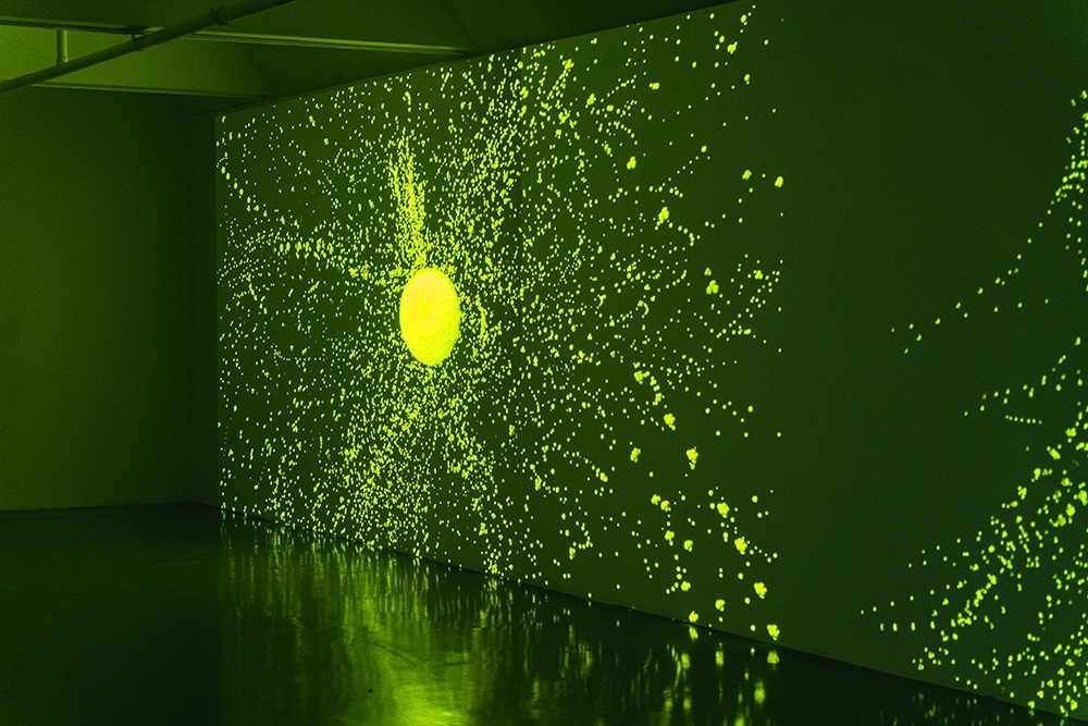 projected green light forms a central circle and splatter pattern on a gallery wall