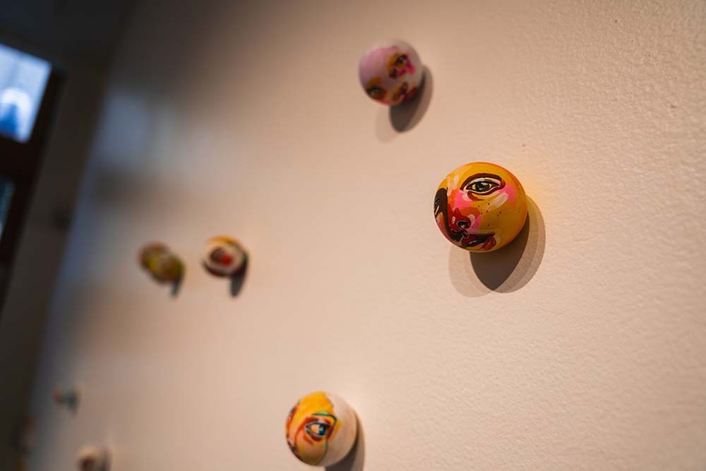 A detail of a wooden sphere painted to look like a face which is attached to a gallery wall