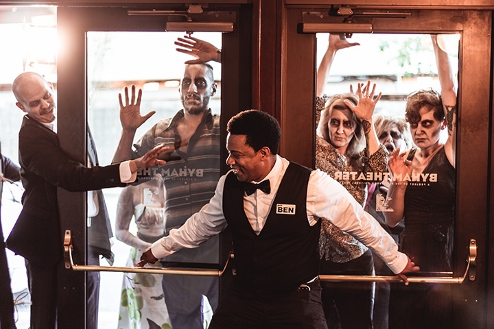 actor portraying ben holds the theater doors close as zombies try to enter