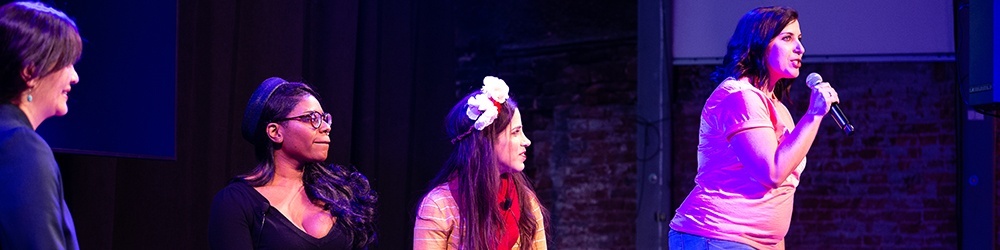 a volunteer addresses the crowd while two authors and a panel moderator look on
