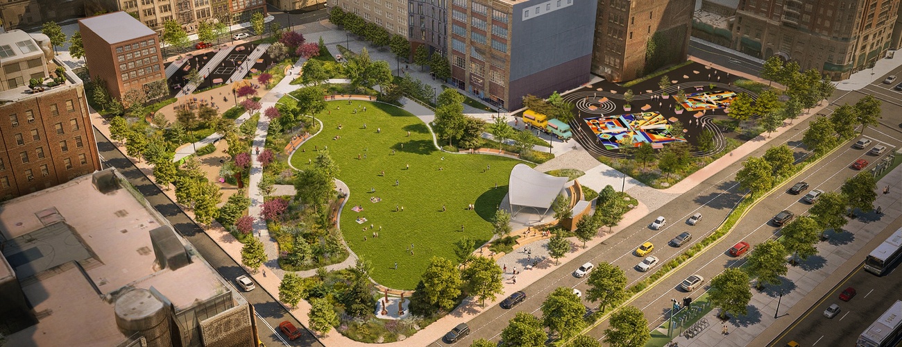 Aerial view of an urban park with a large green lawn, walking paths, scattered trees, colorful playground, and nearby buildings. People are relaxing on the grass and cars are driving on the adjacent road.