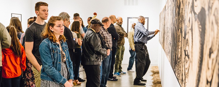 a group of people look at an art piece hanging on the wall
